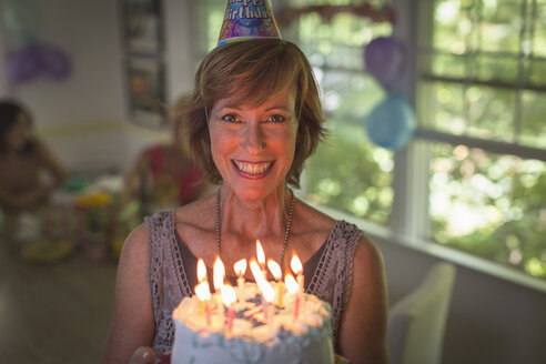 Porträt einer reifen Frau, die einen Geburtstagskuchen mit Kerzen hält - ISF15706