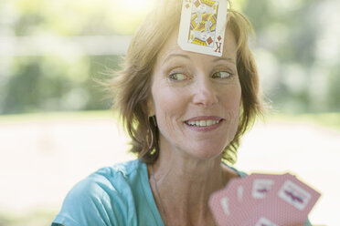 Mature woman playing cards, a playing card stuck on her forehead - ISF15715