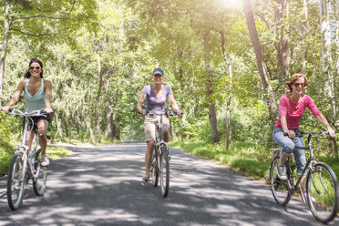 Three mature woman riding bicycles along country road - ISF15720