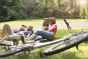 Three mature woman relaxing on grass after bicycle ride - ISF15722