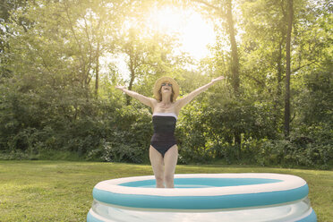Mature woman standing in paddling pool, arms outstretched - ISF15729