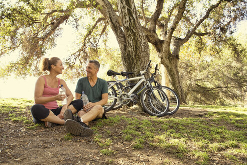 Mature cyclist couple taking a water break in park - ISF15768