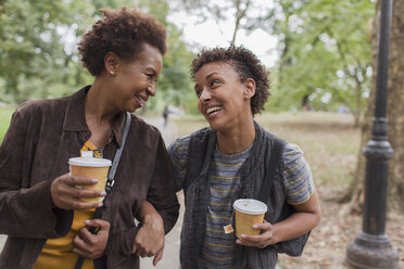 Zwei reife Freundinnen trinken Kaffee zum Mitnehmen, während sie im Park spazieren gehen - ISF15815