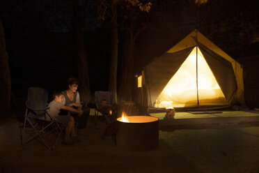 Mature woman and two sons watching campfire at night, County Park, Los Angeles, California, USA - ISF15826