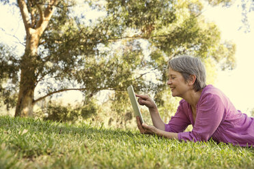 Mature woman using touchscreen on digital tablet in park - ISF15838