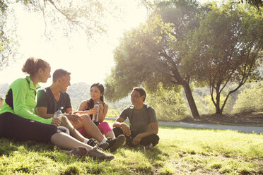 Four mature male and female runners sitting chatting in park - ISF15839