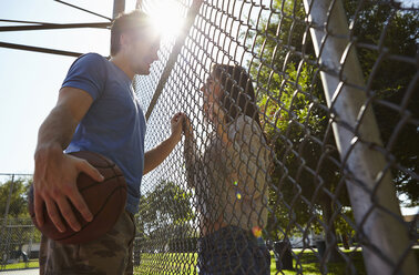 Young couple with basketball standing by wire fence - ISF15865