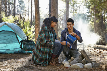 Junges Paar gießt Kaffee am Lagerfeuer im Wald ein, Los Angeles, Kalifornien, USA - ISF15888