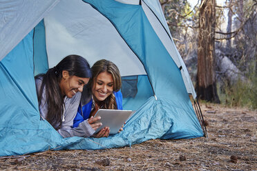 Zwei junge Frauen liegen im Zelt und schauen auf ein digitales Tablet im Wald, Los Angeles, Kalifornien, USA - ISF15895