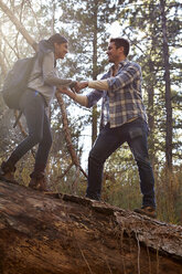 Junger Mann, der seiner Freundin bei einem umgestürzten Baum im Wald hilft, Los Angeles, Kalifornien, USA - ISF15896