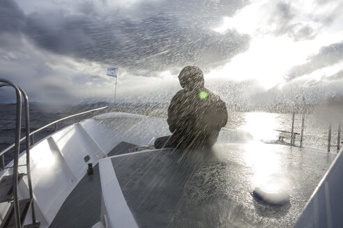 Person in wasserdichter Kleidung vor einem Boot sitzend, das im Regensturm segelt, Ushuaia, Tierra del Fuego, Argentinien - ISF15985