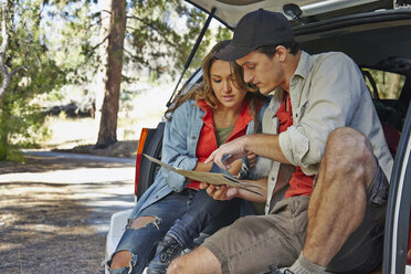 Young couple sitting on car boot pointing at map, Los Angeles, California, USA - ISF15991