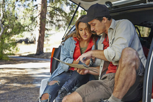 Junges Paar sitzt auf einem Kofferraum und zeigt auf eine Landkarte, Los Angeles, Kalifornien, USA - ISF15991
