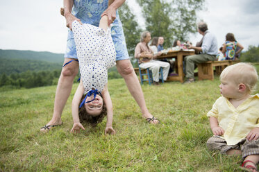 Female family member playfully holding toddler by legs at family gathering, outdoors - ISF16010