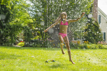 Girl in swimming costume jumping over garden sprinkler - ISF16034