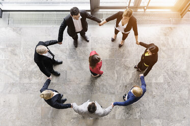 Overhead view of business team in circle holding hands surrounding boss - ISF16170