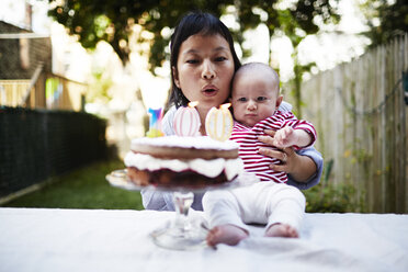 Mother holding baby son, blowing out candles on cake - ISF16202