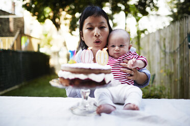 Mutter hält ihren kleinen Sohn und bläst die Kerzen auf dem Kuchen aus - ISF16202