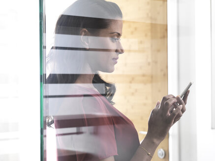 Profile of woman behind glass pane using smartphone - ABRF00201