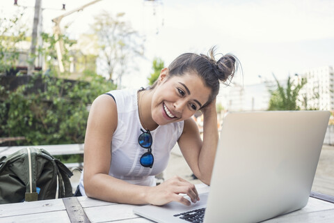 Porträt einer lachenden jungen Frau, die im Freien einen Laptop benutzt, lizenzfreies Stockfoto