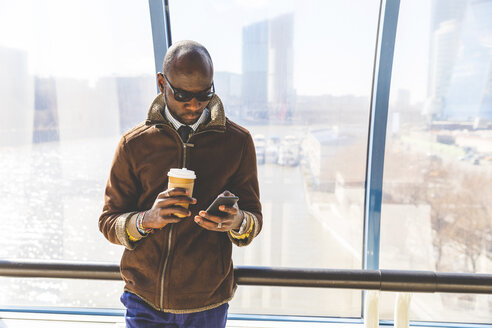 Geschäftsmann mit Kaffee zum Mitnehmen schaut auf sein Smartphone - WPEF00609