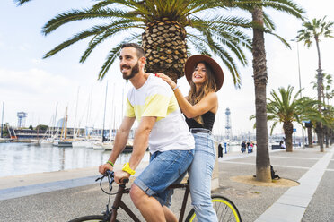 Spain, Barcelona, couple having fun and sharing a ride on a bike together on seaside promenade - WPEF00620