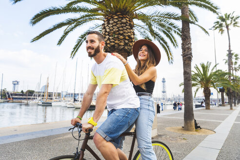 Spanien, Barcelona, Paar, das Spaß hat und gemeinsam auf einem Fahrrad an der Strandpromenade fährt - WPEF00620