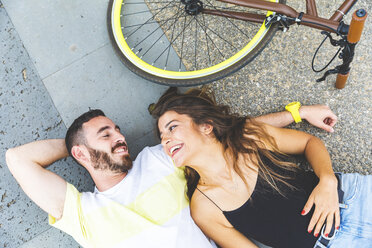 Glückliches Paar liegt auf dem Boden neben dem Fahrrad und lächelt sich gegenseitig an - WPEF00628
