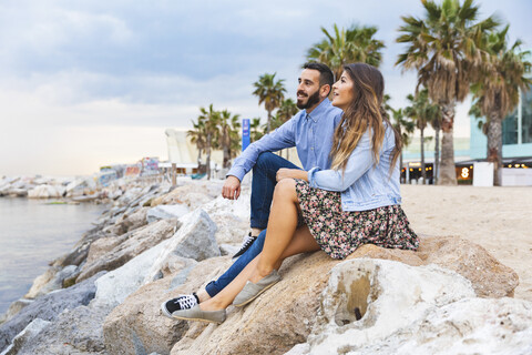 Spain, Barcelona, couple sitting on rocks at the seaside stock photo