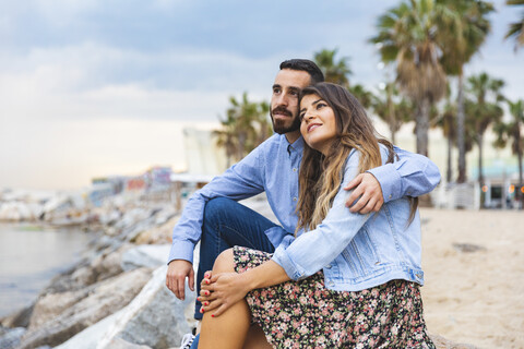 Spain, Barcelona, couple sitting on rocks at the seaside stock photo