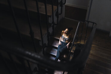 Beautiful young woman sitting in staircase in sunlight - KKAF01134