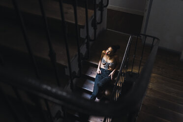 Schöne junge Frau sitzt im Treppenhaus im Sonnenlicht - KKAF01134
