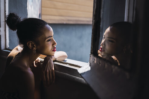 Schöne junge Frau lehnt sich an einen Fensterrahmen, der sich im Spiegel spiegelt - KKAF01137