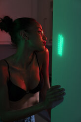 Porträt einer schönen jungen Frau mit BH und Brille in einem dunkel beleuchteten Raum - KKAF01142
