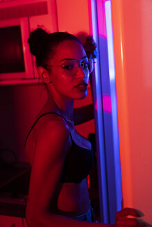 Porträt einer schönen jungen Frau mit BH und Brille in einem dunkel beleuchteten Raum - KKAF01143