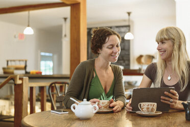 Zwei weibliche Freunde im mittleren Erwachsenenalter, die in einem Café auf dem Lande ein digitales Tablet betrachten - ISF16309