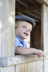 Male toddler in flat cap leaning out of shed window - ISF16340
