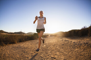 Junge Frau joggt auf einem sonnenbeschienenen Weg, Poway, CA, USA - ISF16354