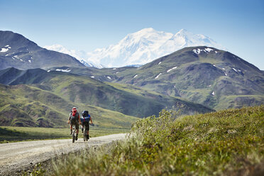Mid adult couple cycling on rural road, Mount McKinley, Denali National Park, Alaska, USA - ISF16385