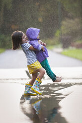 Girl carrying toddler sister through puddle on street - ISF16391