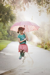 Girl holding up umbrella and jumping puddles on street - ISF16395