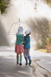 Rear view of boy and girl carrying umbrella on street - ISF16399