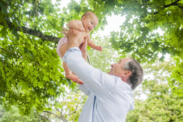 Grandfather lifting up baby granddaughter in park - ISF16406