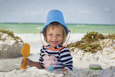 Baby girl with bucket over head on beach, Anna Maria Island, Florida, USA - ISF16408