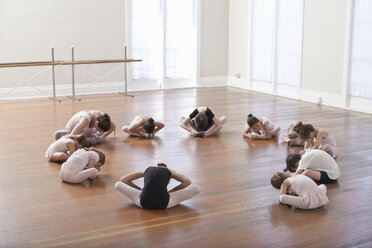 Kinder sitzen auf dem Boden und üben Ballett mit einem Lehrer in einer Ballettschule - ISF16409