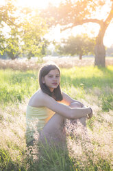 Young girl sitting on meadow at summer evening - LVF07215