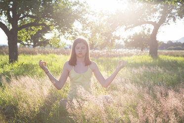 Young girl meditating on meadow at summer evening - LVF07217