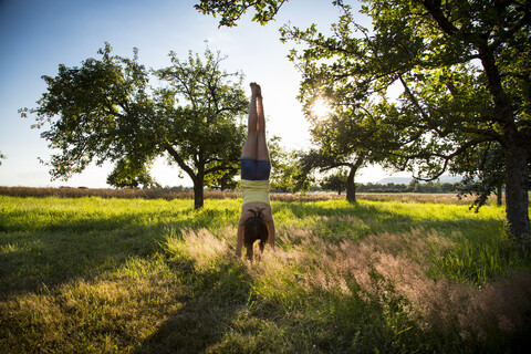 Young girl doing handstand on meadow at summer evening stock photo