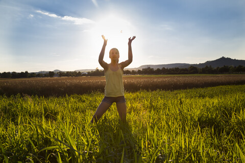 Young girl standing on meadow at summer evening, against the sun, holding sun stock photo