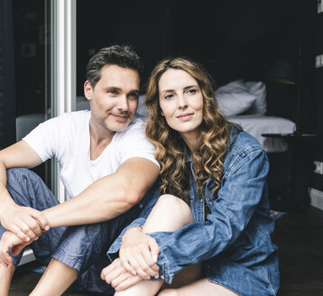 Smiling couple in nightwear at home sitting at French window - UUF14346